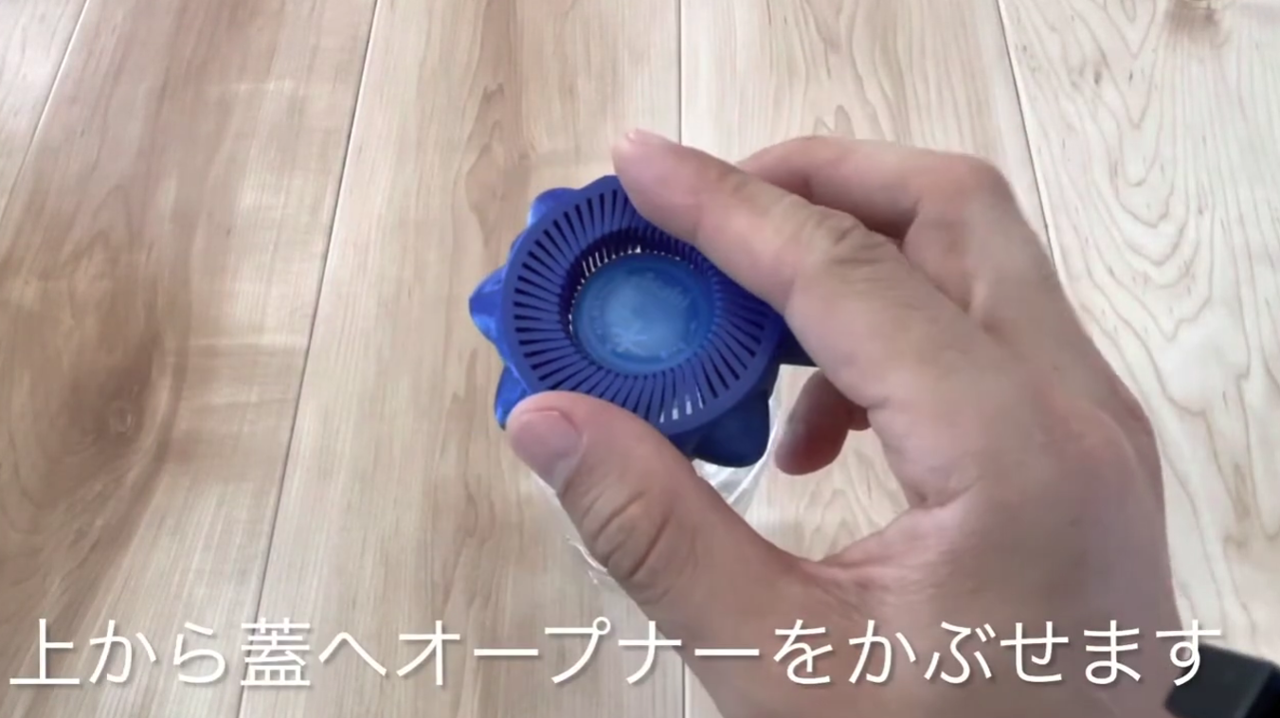 Load video: 上から蓋へオープナーをかぶせます。次に、硬いときは長い柄を壁に押し当てます。あとは親指でクルクル回します。
